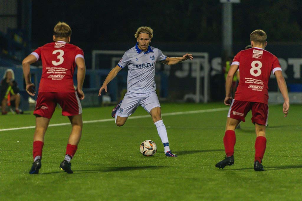 Match action, a player driving forward with the ball between two opponents.